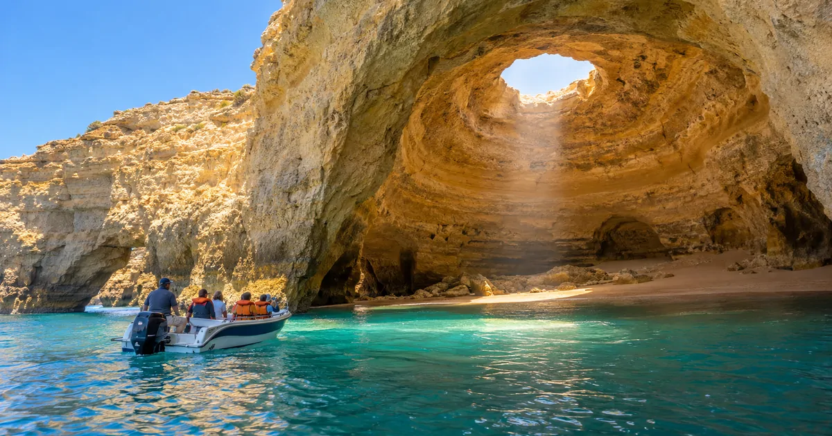 A small speedboat pausing at the western mouth of Benagil cave, with the round skylight and turquoise water inside