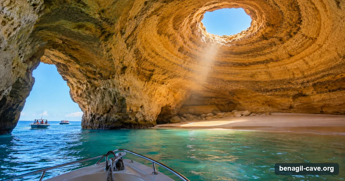 The view from a tour boat paused at the western arch of Benagil Cave: empty beach inside, skylight above, other boats waiting outside